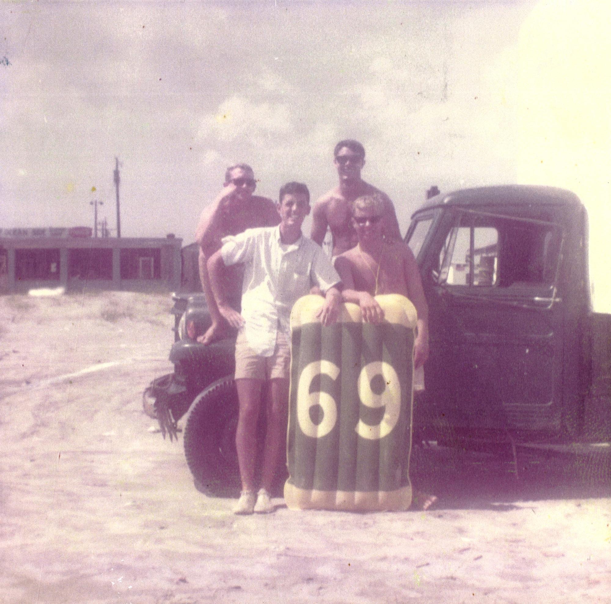 3 men on the beach sitting on the hood of their car